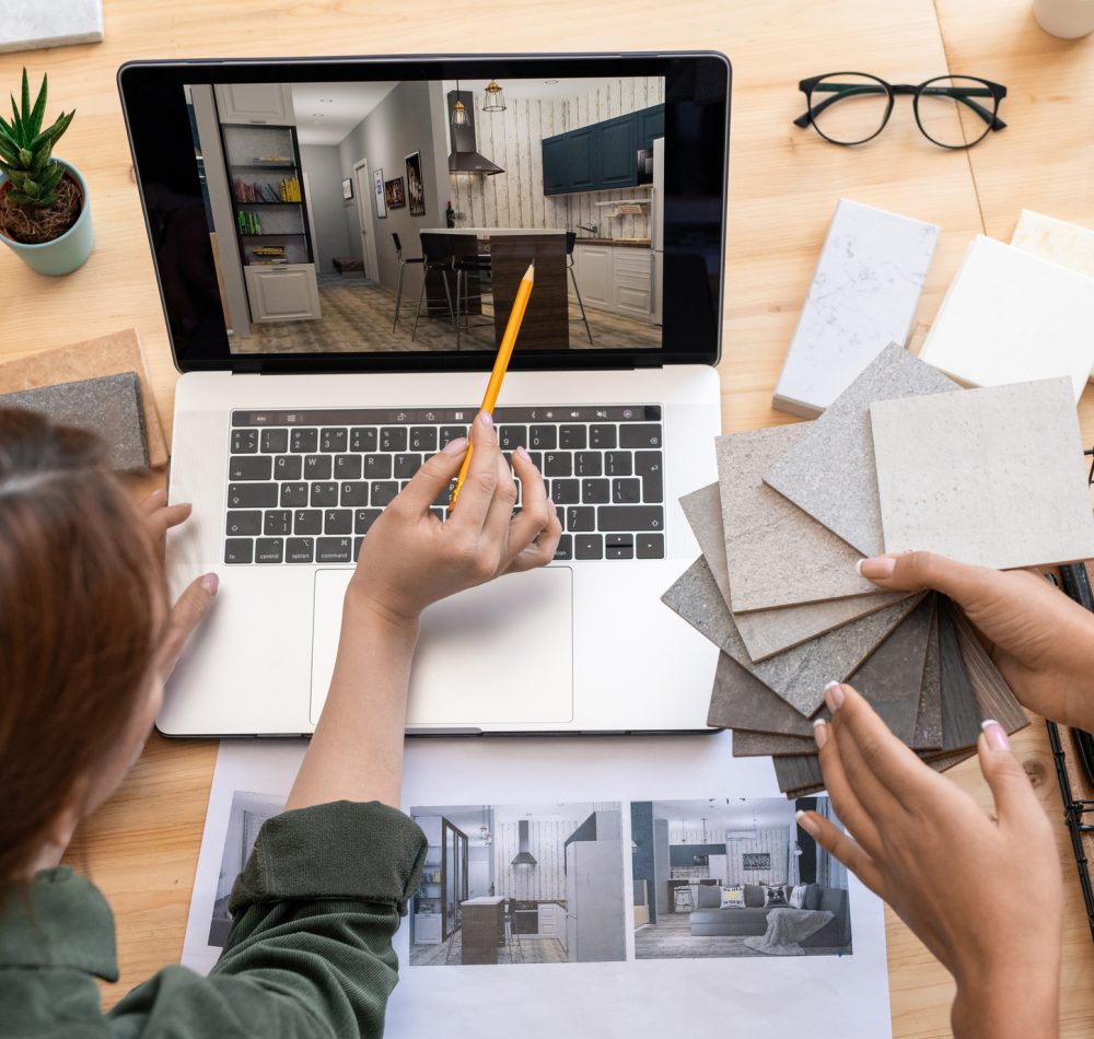 One of young women with pencil pointing at table in the picture of modern room on laptop display while discussing its design with colleague